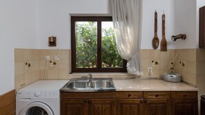 Une cuisine équipée d’un lave-linge, d’un évier, de meubles en bois, d’une fenêtre avec un rideau et d’une radio.