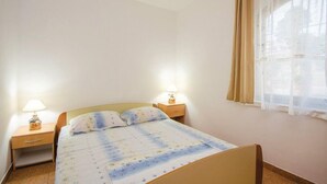 Een slaapkamer met een bed, twee nachtkastjes met lampen, een raam met gordijnen en een effen muur.