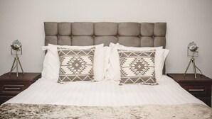 Una cama con cabecera acolchada, dos mesitas de noche con lámparas y almohadas estampadas.