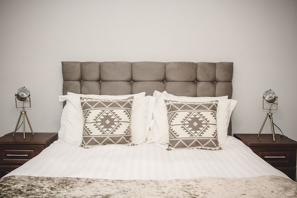 Una cama con cabecera acolchada, dos mesitas de noche con lámparas y almohadas estampadas.