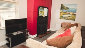 Una sala de estar con televisor de pantalla plana, chimenea, pared de acento roja, un cuadro de barcos y un sofá beige con almohadones.