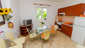 Cocina compacta con comedor, armarios de madera, refrigerador y ventana con vistas a follaje.