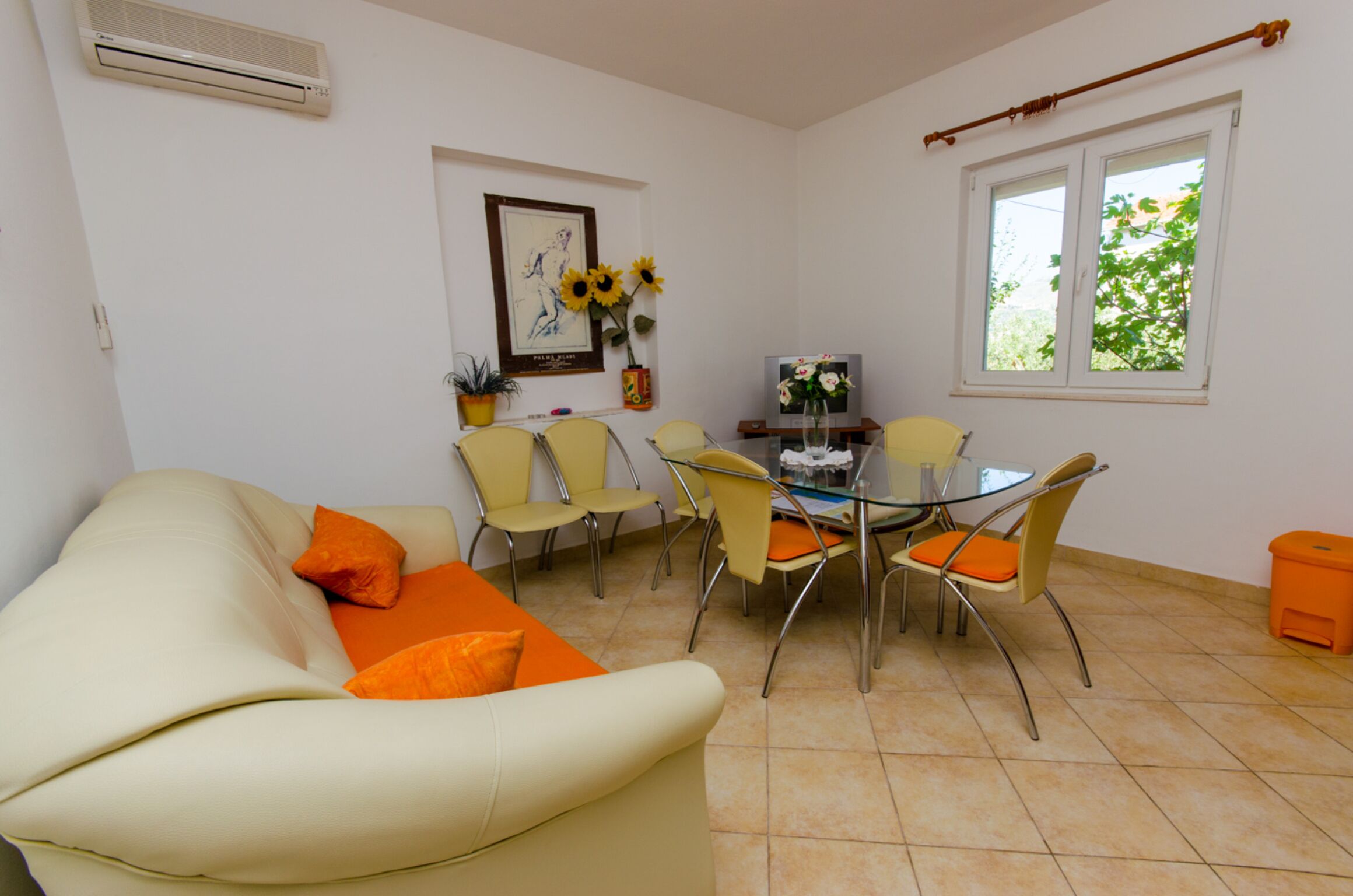 Un salon avec un canapé beige, des fauteuils jaunes, une table en verre et une fenêtre donnant sur un paysage verdoyant.