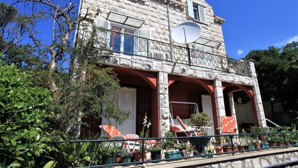 Un edificio de piedra con un balcón, mobiliario exterior y plantas en macetas.
