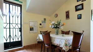 Un comedor con una mesa dispuesta para cuatro, sillas de madera, un jarrón con flores, un reloj y cuadros en la pared.