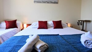 Habitación de hotel con dos camas, ropa de cama roja y blanca, una manta azul y un cuadro con vista al océano.