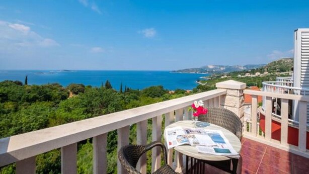 A balcony with a table and chairs overlooking a coastal landscape.