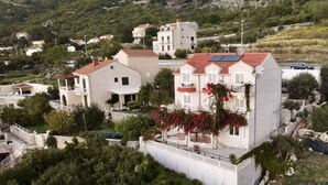 A multi-story building with a red-tiled roof, surrounded by greenery and a mountainous backdrop.