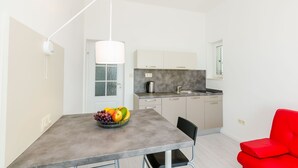 A modern kitchen with a dining table, a red chair, and a bowl of fruit.