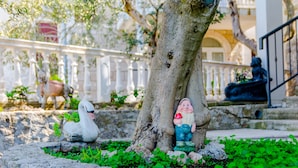 A garden with a swan statue, a tree, and a statue of a man holding a red apple. - Villa Kosa - Two Bedroom Apartment with Balcony and Sea View (Roko) (Brela)