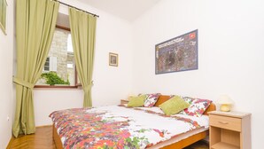 A bedroom with a wooden bed, green curtains, a nightstand with a lamp, and a poster on the wall. - Rooms Lovrijenac - Double Room with Sea View(1) (Dubrovnik)