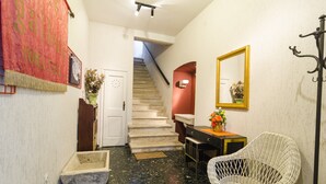 A hallway with a staircase, a white wicker chair, a small table with a vase, and a mirror on the wall. - Rooms Lovrijenac - Double Room with Sea View(1) (Dubrovnik)