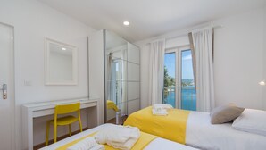 Habitación de hotel con dos camas, un escritorio, una silla, un espejo grande y vista al mar.