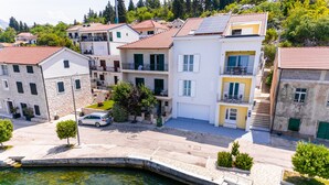 Un área residencial costera con edificios de varios pisos, un paseo pavimentado y un pequeño muelle que se adentra en el agua.