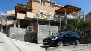 A two-story residential building with a balcony, a car parked in front, and a clear blue sky. - Apartment Brane - Studio Apartment (Mokosica)