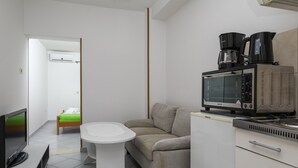 A modern hotel room with a kitchenette, a flat-screen TV, a sofa, a small table, and a bed with a green bedspread. - Apartment Brane - Studio Apartment (Mokosica)
