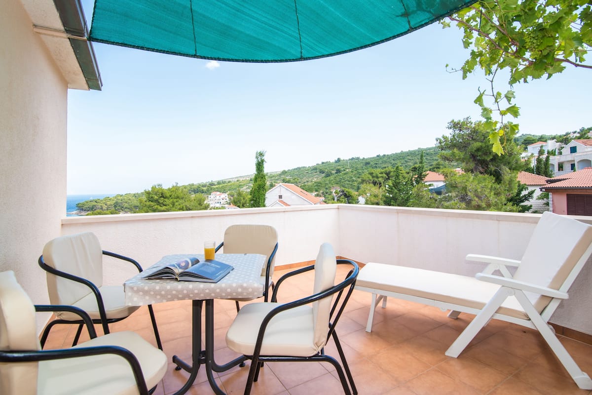 A balcony with a table, chairs, and a sunshade.