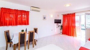 A dining area with a table set for four, a TV mounted on the wall, and a balcony with red curtains.