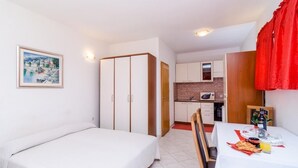 A small, clean room with a bed, a dining table with breakfast, a kitchenette, and a wardrobe.