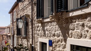 A stone building with multiple windows, some with shutters, and a narrow street with potted plants and a bicycle. - Vivaldi - Comfort Double Room (S2) (Dubrovnik)