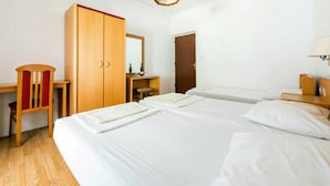 Une chambre d’hôtel avec deux lits, une armoire en bois, un bureau avec une chaise et une petite table avec une bouteille.