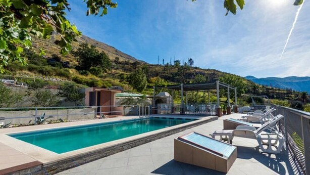 Un espace piscine doté de chaises longues et d’une pergola, entouré de verdure et de collines.