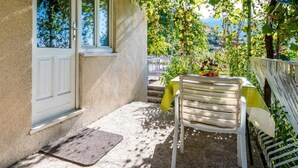 Un petit espace extérieur aménagé avec une chaise et une table, une porte blanche, et une vue sur la verdure et les collines en arrière-plan.