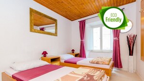 Habitació amb dos llits, ambures de fusta, un mirall, una finestra amb cortines i un ram de flors en un vas.