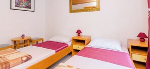 Una habitación con dos camas, cabeceros de madera, un espejo, mesitas de noche y un cuadro enmarcado en la pared.