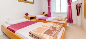Una habitación con dos camas, cabeceros de madera, un espejo, una ventana con cortinas y un jarrón con ramas.