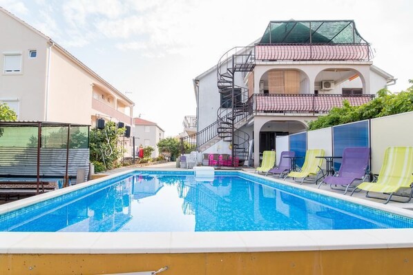 A swimming pool with lounge chairs and a multi-story building with balconies.