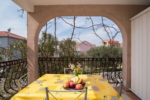 A balcony with a table set for a meal, surrounded by a metal railing and a view of neighboring houses.