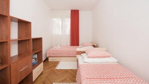 A small, neatly organized bedroom with two single beds, a wooden wardrobe, and a window with sheer curtains. - Apartment H&M (ST) - Two Bedroom Apartment with Balcony (Split)