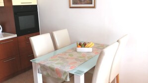 A dining area with a table set for four, a fruit bowl on the table, and a kitchen area with cabinets and an oven to the left. - Apartment H&M (ST) - Two Bedroom Apartment with Balcony (Split)