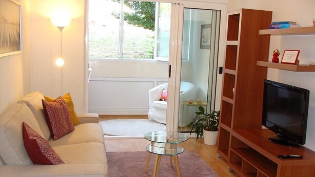 A living room with a white sofa, glass coffee table, wooden TV stand, and a sliding glass door leading to a balcony. - Apartment H&M (ST) - Two Bedroom Apartment with Balcony (Split)