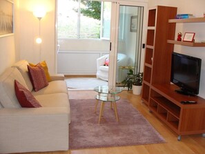 A living room with a white sofa, glass coffee table, wooden TV stand, and a sliding glass door leading to a balcony. - Apartment H&M (ST) - Two Bedroom Apartment with Balcony (Split)