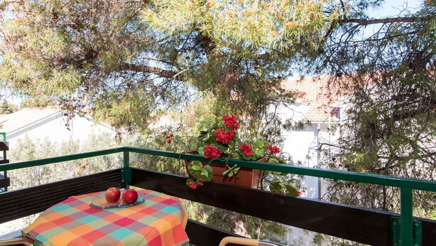 Een balkon met een tafel gedekt voor twee personen, een stoel en een potplant met rode bloemen.
