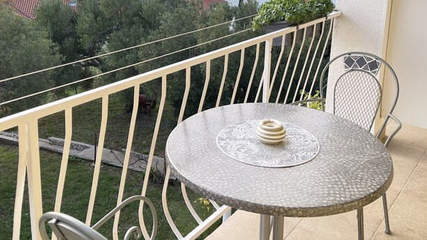 Un balcón con una mesa redonda y sillas, con vista a una masa de agua y terreno distante.