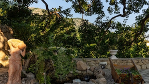 Un jardín con una estatua, un muro de piedra y un macetero de madera con flores.