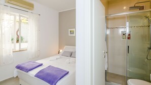 Un dormitorio con cama, un baño con ducha y una ventana con cortinas.