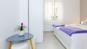 Una habitación de hotel con una cama, una mesita con una planta en maceta y una ventana con cortinas translúcidas.