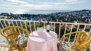 A balcony with wicker chairs and a table, overlooking a coastal town.
