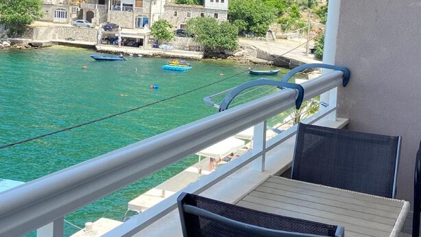 Balcón con dos sillas y una mesa con vista a una zona costera con barcos y edificios.