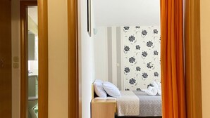 Una habitación con cama, mesita de noche y un baño visible a través de una puerta abierta.