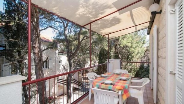 Un balcón con mesa lista para comer, sillas blancas y vistas a árboles y edificios.