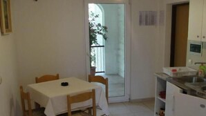 Una cocina pequeña y limpia con una mesa de comedor y sillas, un refrigerador y un puerta corrediza de vidrio que da a un balcón.