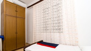 Un dormitorio con un armario de madera, una cama con manta blanca y roja, y una cortina ligera con estampado floral.