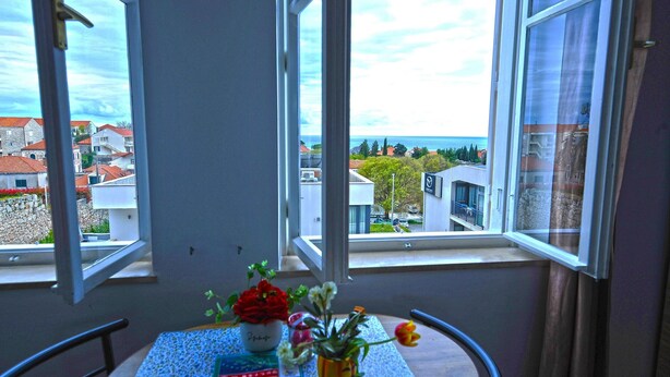 A balcony with a table, two potted plants, and a view of the sea and buildings. - Villa Katarina - Double Room with Sea View (First Floor) (Dubrovnik)