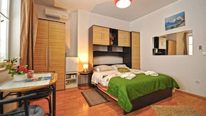 A bedroom with a bed, a table with a chair, a small table with a lamp, and a window with curtains. - Villa Katarina - Double Room with Sea View (First Floor) (Dubrovnik)