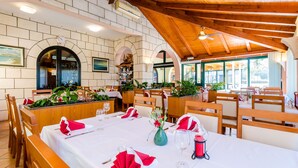 Ein Restaurant mit Holzbalken, weißen Wänden und Rundbogenöffnungen. Die Tische sind mit roten Servietten und weißen Tischdecken gedeckt.